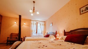 Une chambre d’hôtel avec deux lits, une tête de lit en bois, un lustre, une chaise et une fenêtre avec des rideaux.