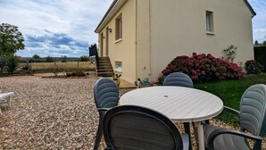 Ein Haus mit Kiesweg, einem runden Tisch mit Stühlen und einem kleinen Garten mit rosa Blumen.