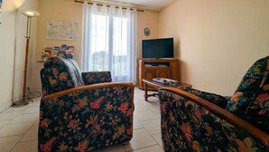Ein Wohnzimmer mit floral gemusterten Sesseln, einem Holzschrank mit Fernseher und einer Karte an der Wand.