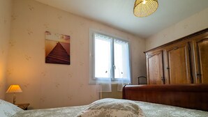 Ein Schlafzimmer mit einem Bett, einem Fenster, einer Heizung, einer Lampe und einem Holzschrank.