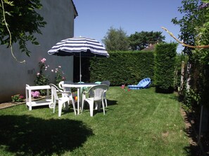 Ein Garten mit einem weißen Tisch und Stühlen, einem gestreiften Sonnenschirm und einem blauen aufblasbaren Pool.