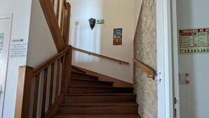 Eine Holzt Treppe mit Handlauf, einer an der Wand montierten Notleuchte und einem Brandschutzplakat.