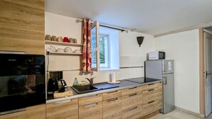 A modern kitchen with wooden cabinets, a built-in oven, a microwave, and a window with a curtain. - Family-Friendly Cottage in Brenne Park with Bikes, BBQ & Near Lake! (Luant)