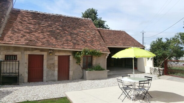 A house with a tiled roof, a patio with a table and chairs, and a yellow umbrella. - Family-Friendly Cottage in Brenne Park with Bikes, BBQ & Near Lake! (Luant)