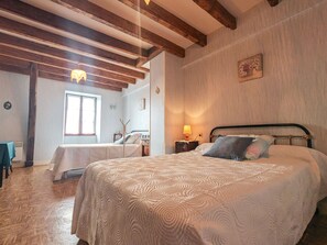 A bedroom with two beds, wooden beams, a window, and a wall-mounted lamp.