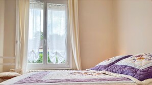 A bedroom with a bed, a window with curtains, and a view of greenery outside. - Charming Townhouse with Garden, Near Downtown Châteauroux (Châteauroux)