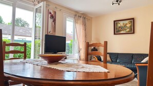 A dining area with a wooden table, chairs, a television, and a sofa. - Charming Townhouse with Garden, Near Downtown Châteauroux (Châteauroux)