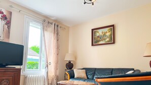 A living room with a sofa, a television, a table, and a painting on the wall. - Charming Townhouse with Garden, Near Downtown Châteauroux (Châteauroux)