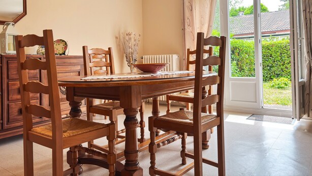 A dining area with a wooden table, chairs, a bowl, a vase with dried flowers, and a view of greenery outside. - Charming Townhouse with Garden, Near Downtown Châteauroux (Châteauroux)