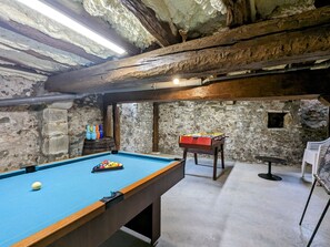 A pool table with balls, a foosball table, and a billiards table in a room with stone walls and wooden beams. - Family-Friendly Medieval House with Game Room Near Château de Valençay (Levroux)