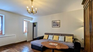 A living room with a sofa, a wooden coffee table, a chandelier, a framed picture on the wall, and a door leading to another room.