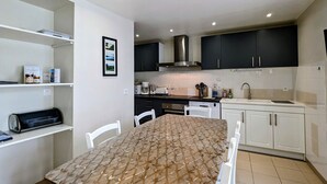 A compact kitchen with white cabinets, a black range hood, and a dining table with a patterned tablecloth.