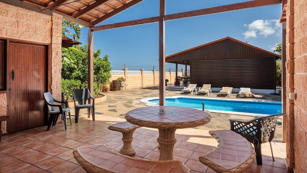 A covered patio with a pool, outdoor seating, and a view of the pool area.
