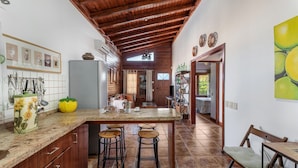 A kitchen with a wooden ceiling, a central island with stools, and a dining area with a chair.