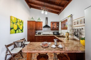A kitchen with wooden cabinets, a granite countertop, a coffee maker, and a large painting of lemons. - Vacation Home "La Molineta" with Mountain View, Pool, Garden, Terrace & Wi-Fi (La Hidalga Arafo)