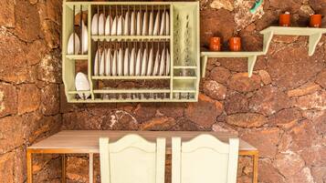 Una cocina rústica con pared de piedra, una mesa de madera y una estantería con platos y tazas.