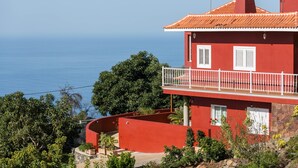 Een rood gebouw met een balkon, een stenen muur en uitzicht op zee.