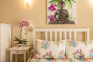 Ein Schlafzimmer mit einem Bett, einem Nachttisch, einer Topfpflanze und einer an der Wand befestigten Buddha-Statue.