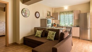 Een moderne woonkamer met een bank, een eethoek en een keuken met houten kasten en een roestvrijstalen koelkast.