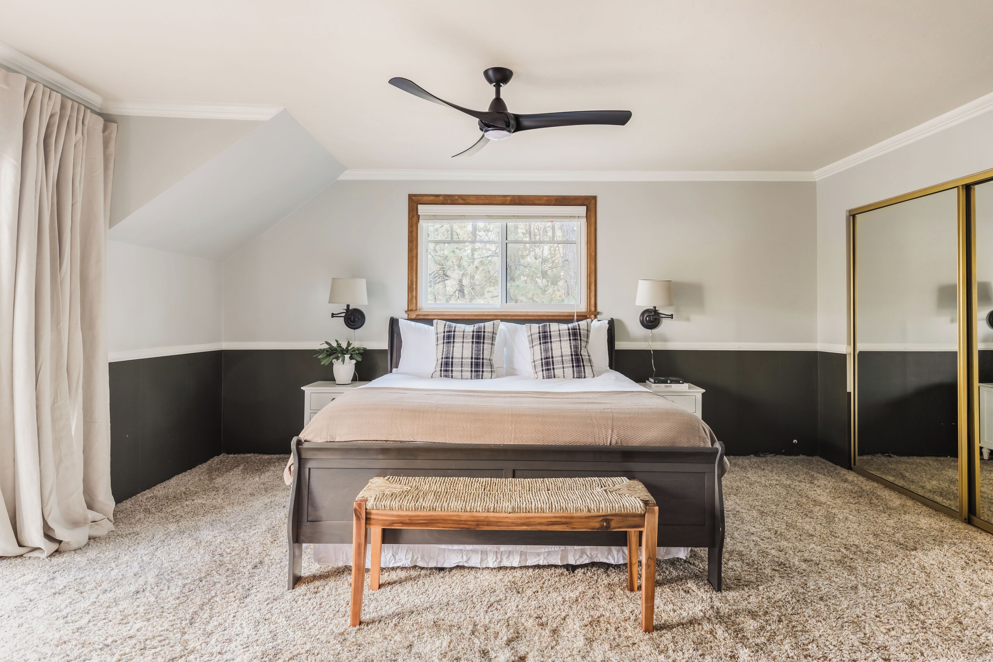 A bedroom with a bed, bedside lamps, a ceiling fan, a window, and a large mirror.
