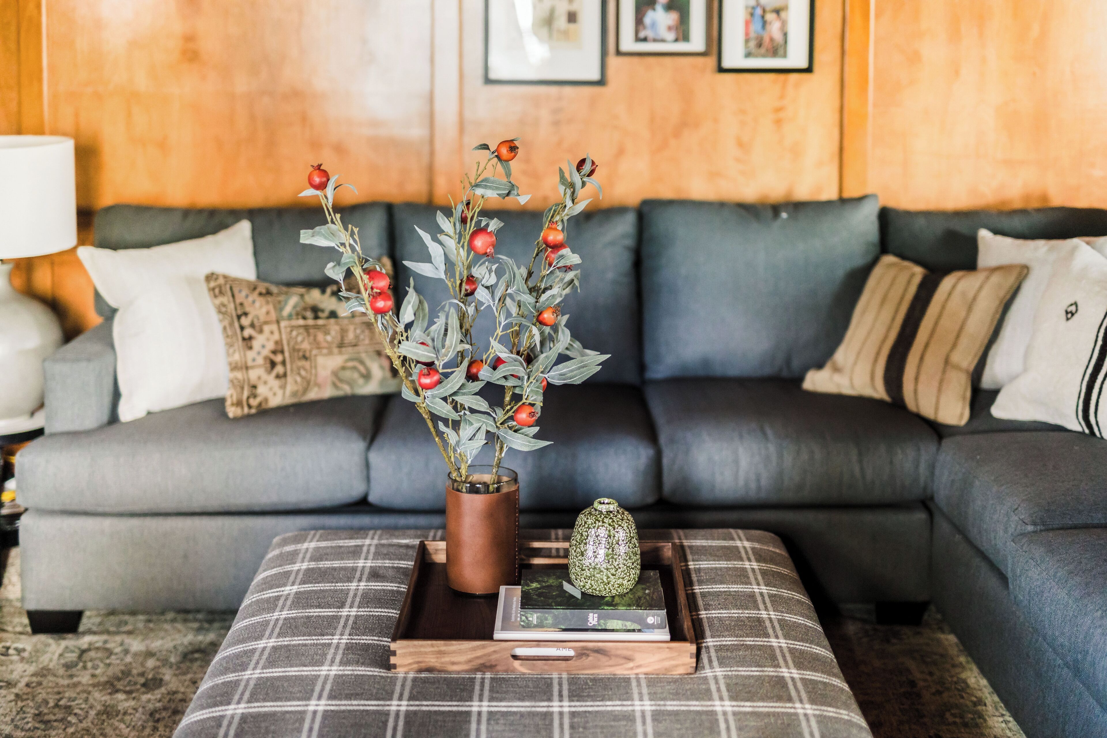 Una sala de estar con un sofá gris, una mesa de centro con un libro y un objeto decorativo, y un florero con bayas rojas sobre una bandeja de madera.