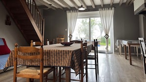 Een eetruimte met een houten tafel en stoelen, een trap en uitzicht door een raam.