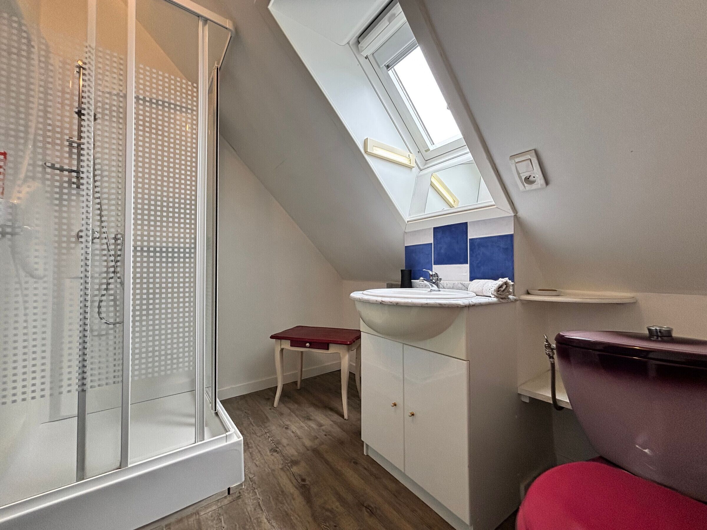A bathroom with a shower, a sink, a small table, and a red chair.