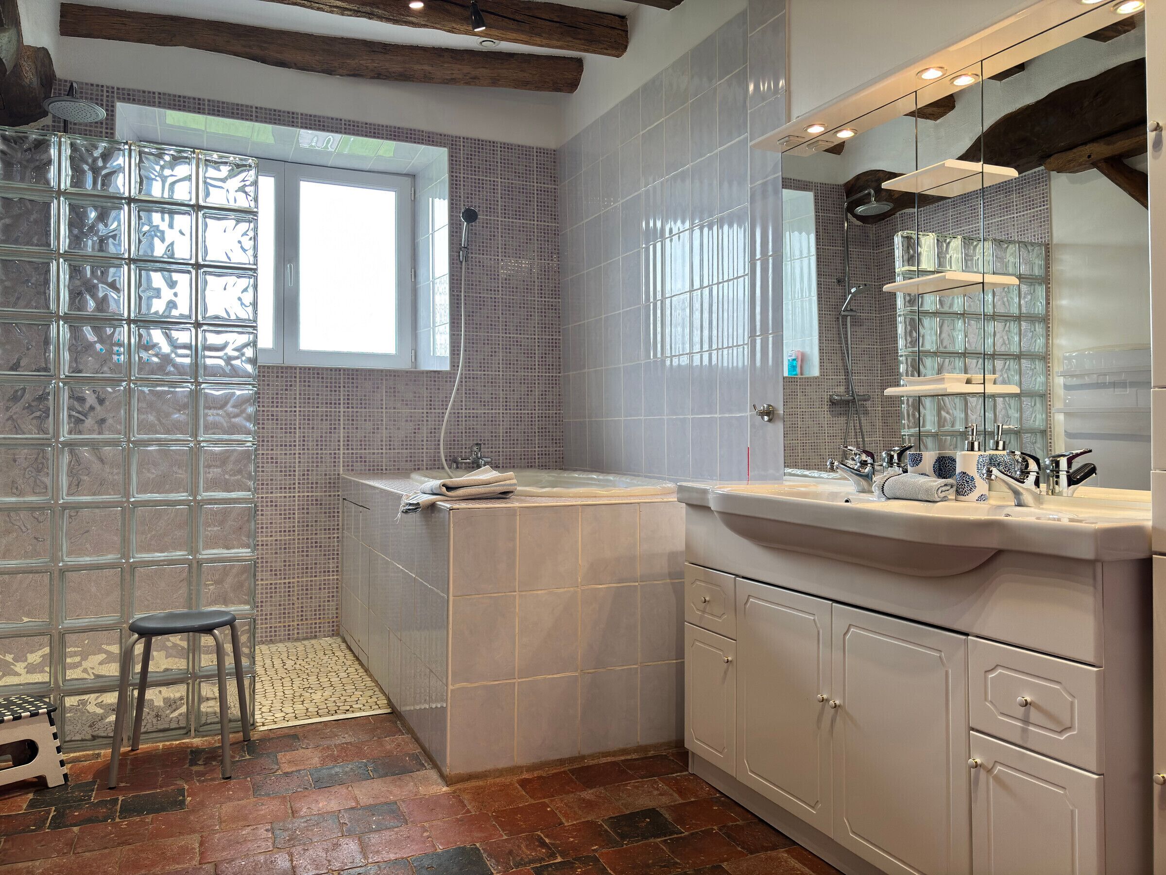 Une salle de bain avec une douche à parois de verre, une baignoire, un lavabo avec un miroir et un tabouret.