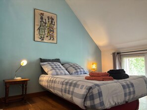 Une chambre à coucher avec un lit, une lampe de chevet, un tableau accroché au mur et une fenêtre avec des rideaux.