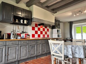 Een keuken met donkere kastjes, een rood-wit geruit spatwand, en een zithoek met een tafel en stoelen.
