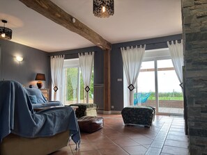 Une pièce comprenant un lit, une chaise, une table avec une lampe et offrant une vue sur l’extérieur grâce à de grandes fenêtres.