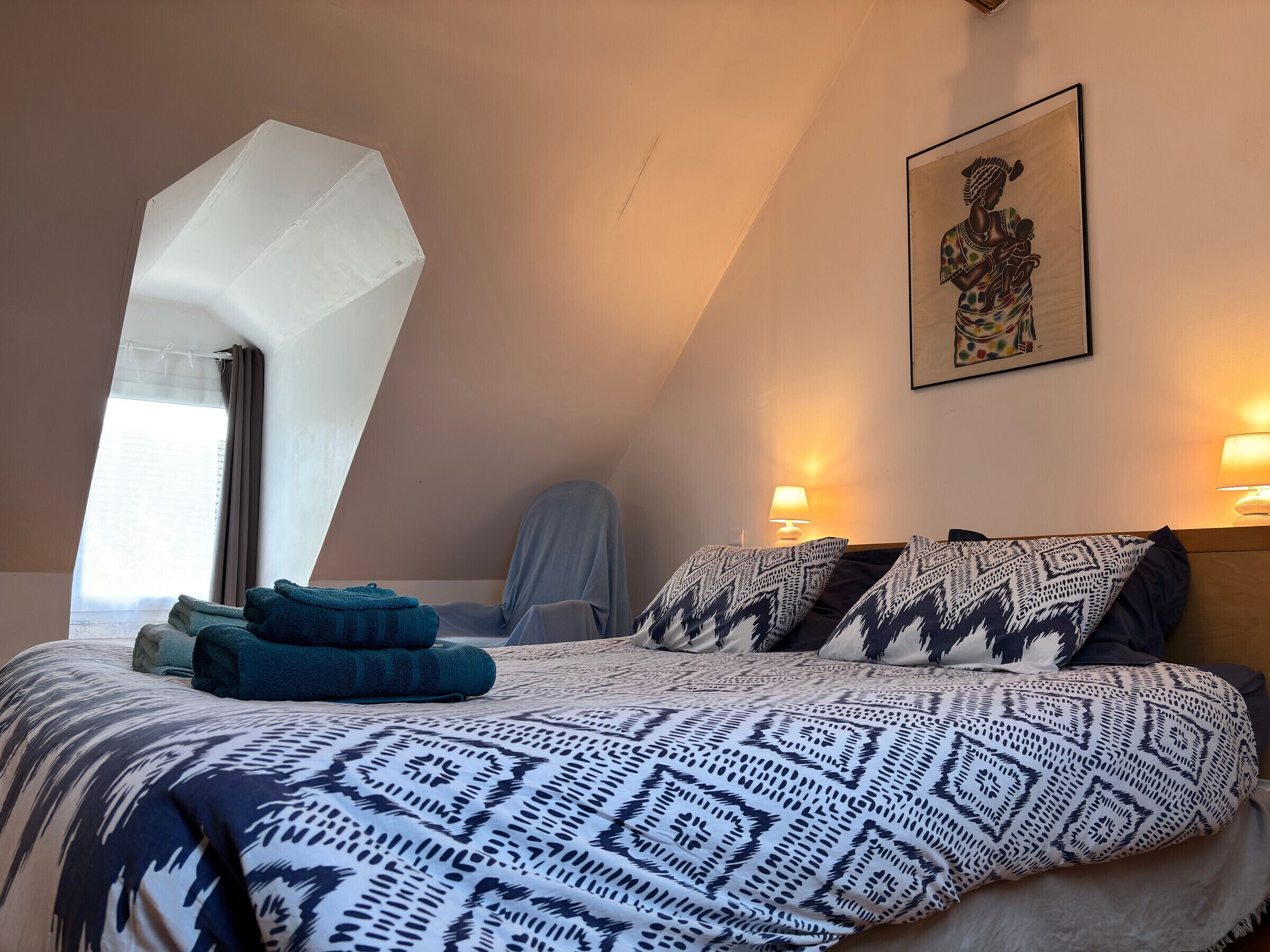 A bedroom with a large bed, a painting on the wall, and a window with curtains.