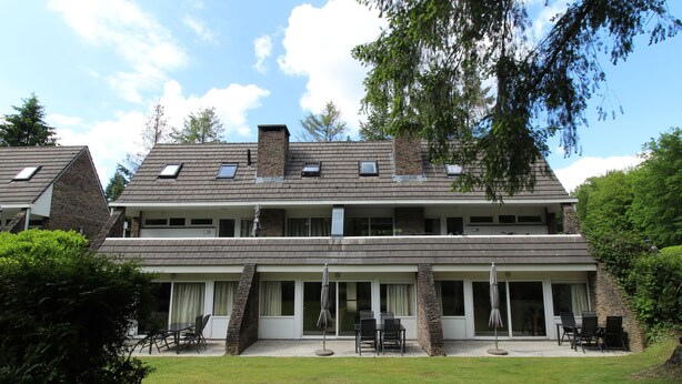 Un bâtiment à deux étages, doté d’un toit plat, de grandes fenêtres et d’un patio couvert aménagé avec du mobilier d’extérieur.