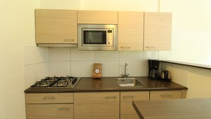Une cuisine avec des meubles de rangement en bois, un four à micro-ondes, une cuisinière à gaz, un évier et une machine à café.