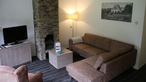 Un salon avec une cheminée en briques, un canapé, un téléviseur posé sur un meuble et une lampe.