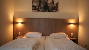 Un lit double avec une literie blanche, deux tables de chevet avec des lampes et un tableau encadré au mur.
