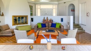 A spacious living room with a high ceiling, a wooden coffee table, and a sofa with colorful cushions.