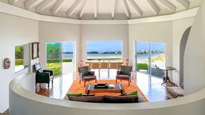 A spacious living area with a view of a lake, a piano, and a dining table with chairs.