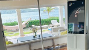A room with a view of a body of water, a weightlifting area with barbells and weights, and a white cabinet with a screen displaying workout metrics.