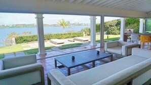 A covered outdoor seating area with a view of the water, a patio table, and a sofa.