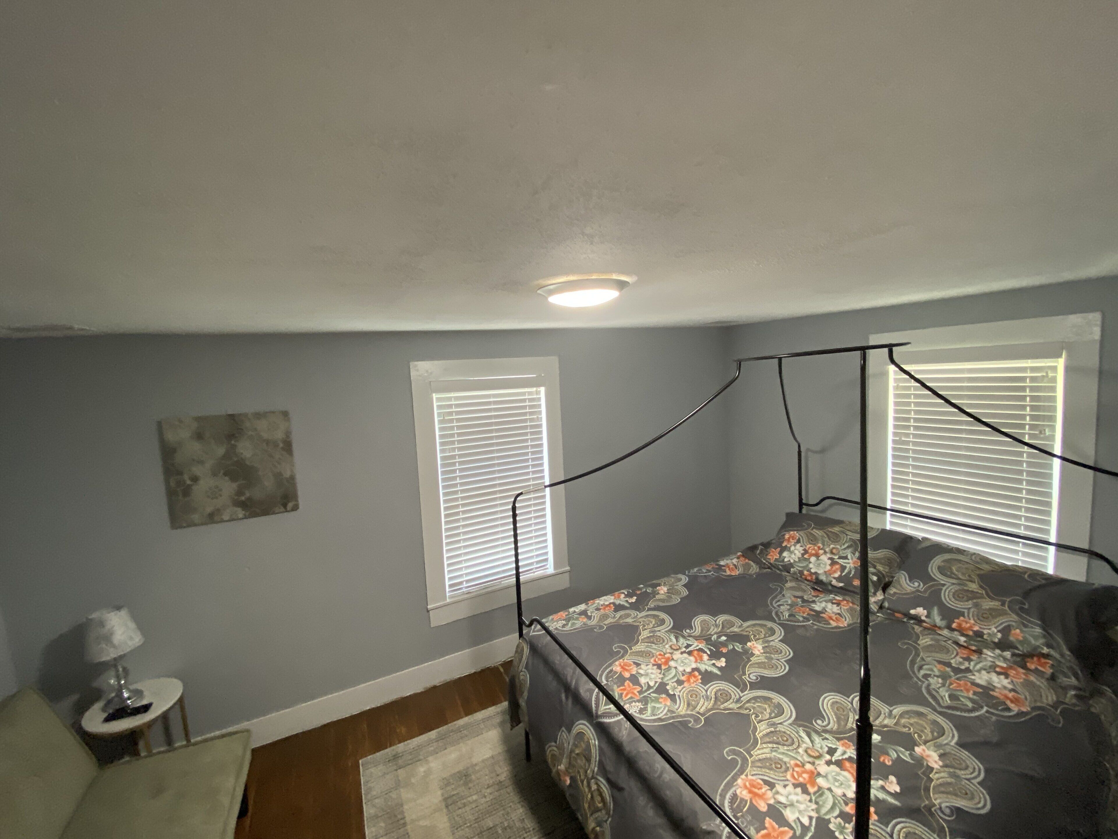 A bedroom with a four-poster bed, a small side table, and a wall-mounted lamp.