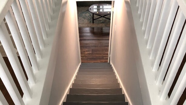 Eine Treppe mit weißen Geländern und einem dunklen Holzboden, die zu einem Raum mit Tisch und Stühlen führt.