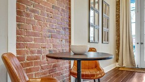 A dining area with a brick wall, a round table with a bowl, and leather chairs. - Stylish 1BR LGD condo with private balcony on Magazine St. King bed, chef’s kitchen, Wi-Fi, walk to cafés. (New Orleans)