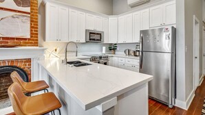 A modern kitchen with white cabinets, a stainless steel refrigerator, a microwave, and a sink with a faucet. - Stylish 1BR LGD condo with private balcony on Magazine St. King bed, chef’s kitchen, Wi-Fi, walk to cafés. (New Orleans)