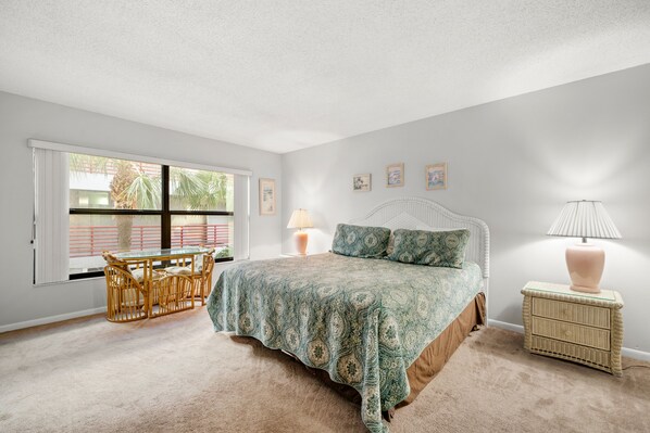 A bedroom with a bed, a small table, a lamp, and a window with a view of palm trees. - Sandy Shores 107 Side Unit on the Beach (Madeira)
