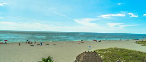 A beach with thatched umbrellas and lounge chairs, a clear sky, and the ocean.