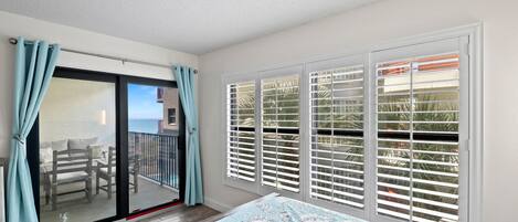 A bedroom with a balcony, a bed with a patterned bedspread, and a view of the ocean through the balcony doors.