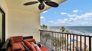 Un balcón con vista a la playa, un ventilador de techo y mobiliario exterior.