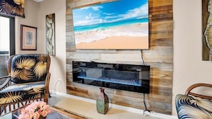 Una sala de estar con un televisor de pantalla plana grande montado en una pared de madera, una chimenea debajo y un jarrón decorativo en el suelo.