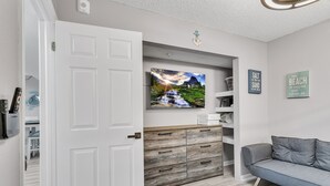A modern living room with a grey sofa, a flat-screen TV mounted above a wooden cabinet, and a blue patterned rug. - Sandy Shores 311 Water View 2 BR (Madeira Beach)